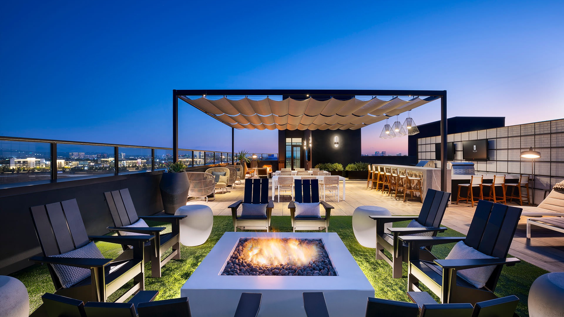 chairs surround fire pit on rooftop lounge at night